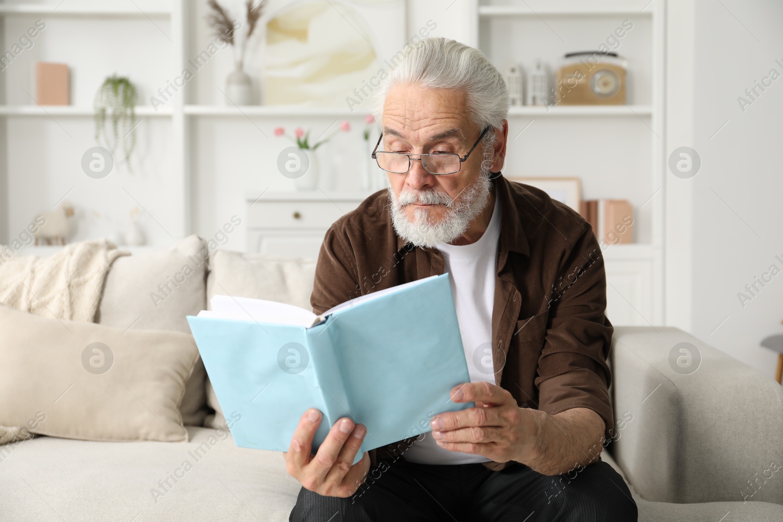 Senior man with vision problem reading book on sofa at home Photo of Senior man with vision problem reading book on sofa at home