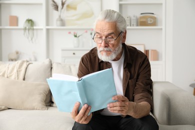 Photo of Senior man with vision problem reading book on sofa at home