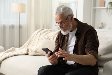 Photo of Senior man with vision problem using smartphone on sofa at home, space for text