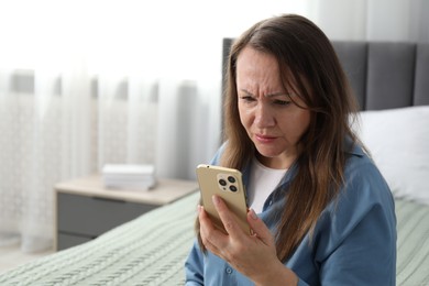 Photo of Woman with vision problem using smartphone on bed at home, space for text