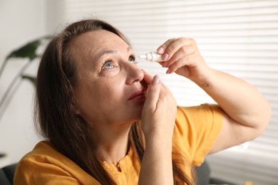 Photo of Woman applying eye drops near window at home