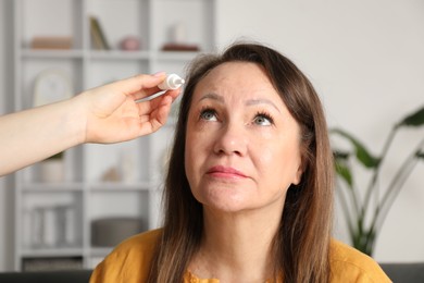 Photo of Daughter dripping medication into mother's eye at home, closeup