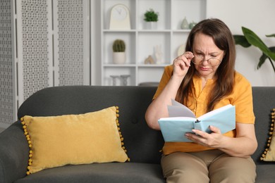 Photo of Woman with vision problem reading book on sofa at home