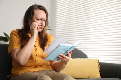 Photo of Woman with vision problem reading book on sofa at home, space for text