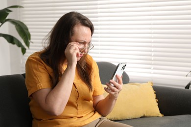 Photo of Woman with vision problem using smartphone on sofa at home, space for text