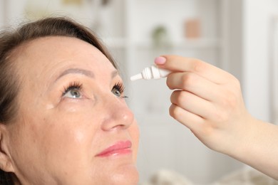 Photo of Daughter dripping medication into mother's eye at home, closeup