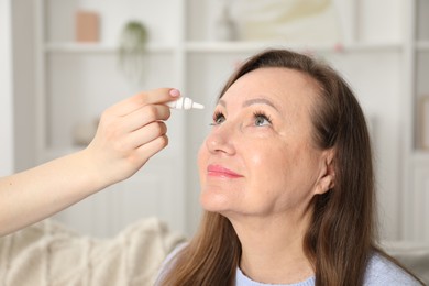 Photo of Daughter dripping medication into mother's eye at home, closeup