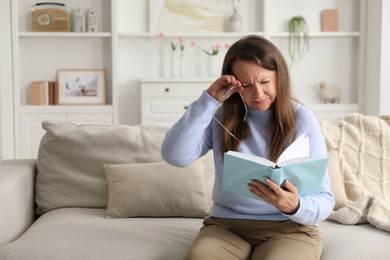 Photo of Woman with vision problem reading book on sofa at home, space for text