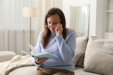 Photo of Woman with vision problem reading book on sofa at home