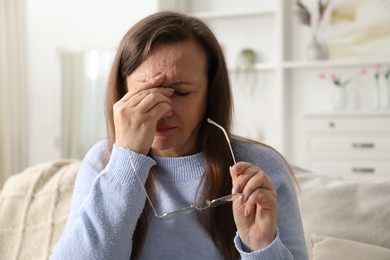 Photo of Woman with glasses suffering from eyestrain on sofa at home