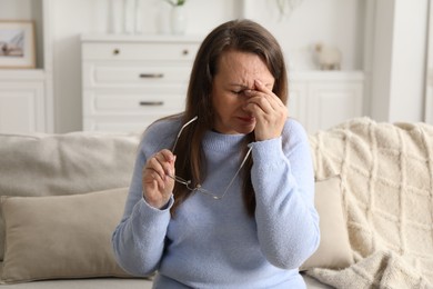 Photo of Woman with glasses suffering from eyestrain on sofa at home