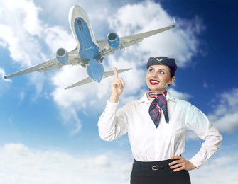 Image of Smiling stewardess pointing at plane in blue sky with and clouds