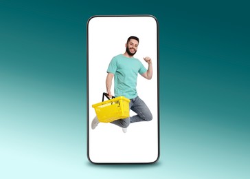 Image of Happy man with shopping basket jumping out of mobile phone on teal gradient background. Online ordering