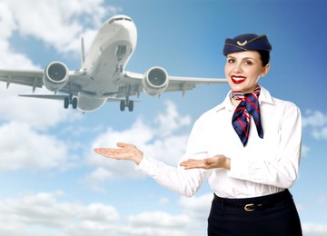 Image of Smiling stewardess pointing at plane against blue sky with clouds