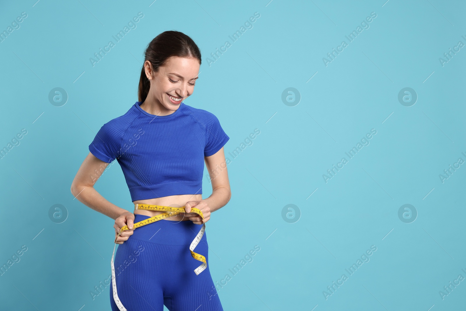 Photo of Beautiful woman measuring her belly with tape on light blue background, space for text