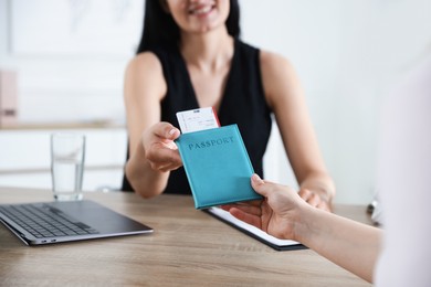 Photo of Travel agent giving passport with ticket to woman at wooden table in office, closeup