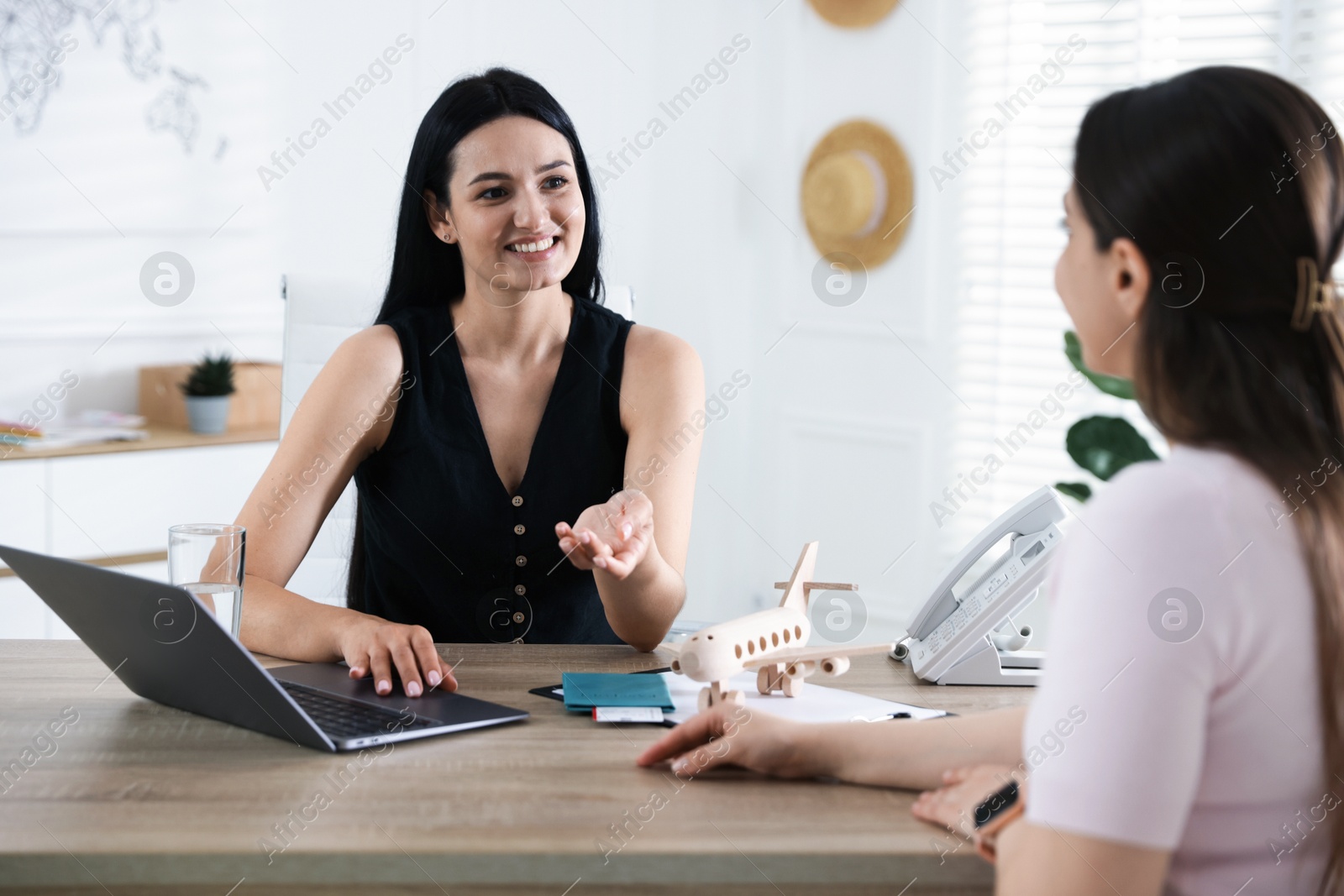 Woman planning vacation with travel agent at wooden table in office Photo of Woman planning vacation with travel agent at wooden table in office