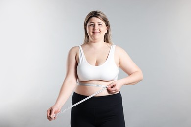 Photo of Weight loss. Plus size woman measuring waist with tape on gray background