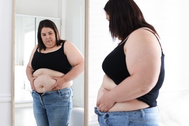 Photo of Woman with excessive belly fat near mirror indoors. Overweight problem