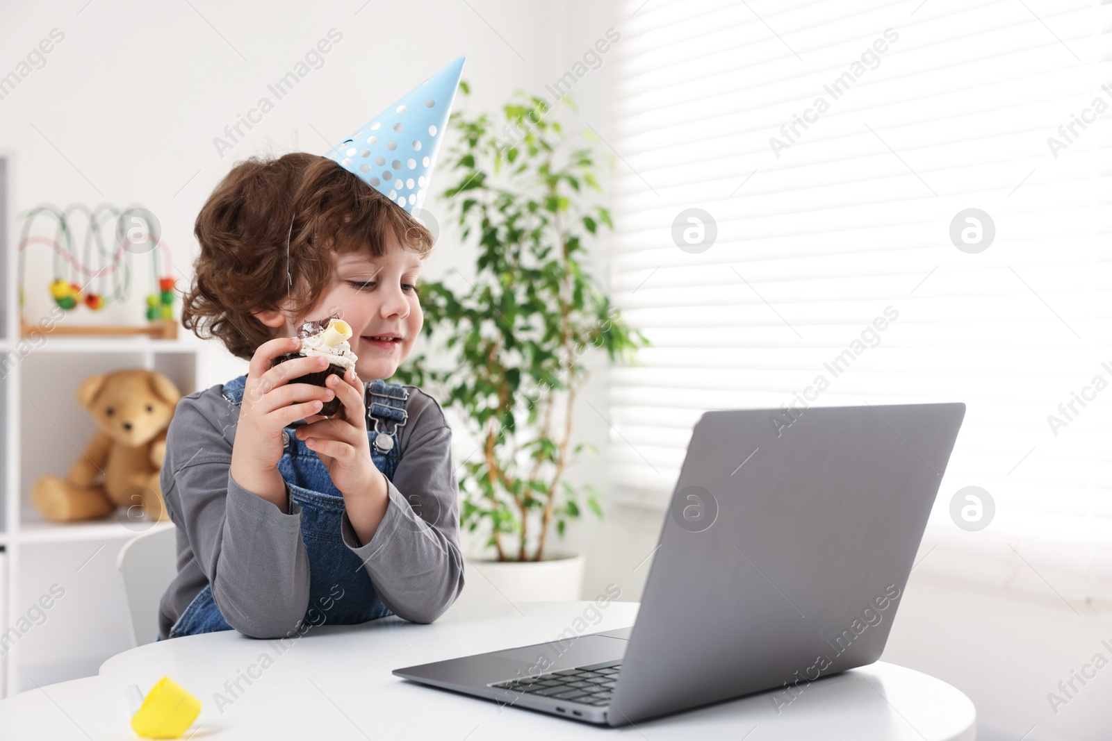 Birthday celebration. Little boy with cupcake having video call via laptop at table indoors. Space for text Photo of Birthday celebration. Little boy with cupcake having video call via laptop at table indoors. Space for text