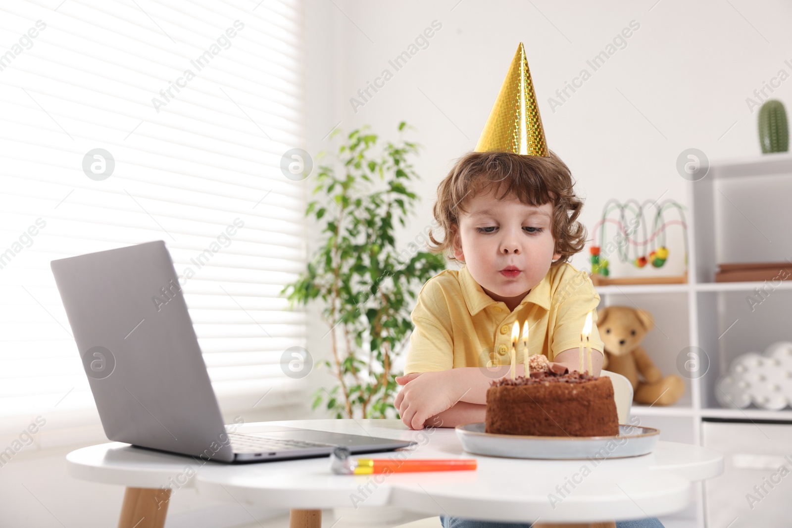 Birthday celebration. Little boy blowing candles on cake while having video call via laptop at table indoors. Space for text Photo of Birthday celebration. Little boy blowing candles on cake while having video call via laptop at table indoors. Space for text