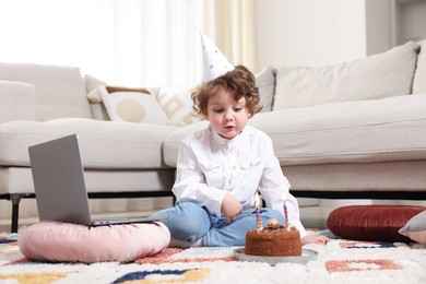 Photo of Birthday celebration. Little boy with cake having video call via laptop at home