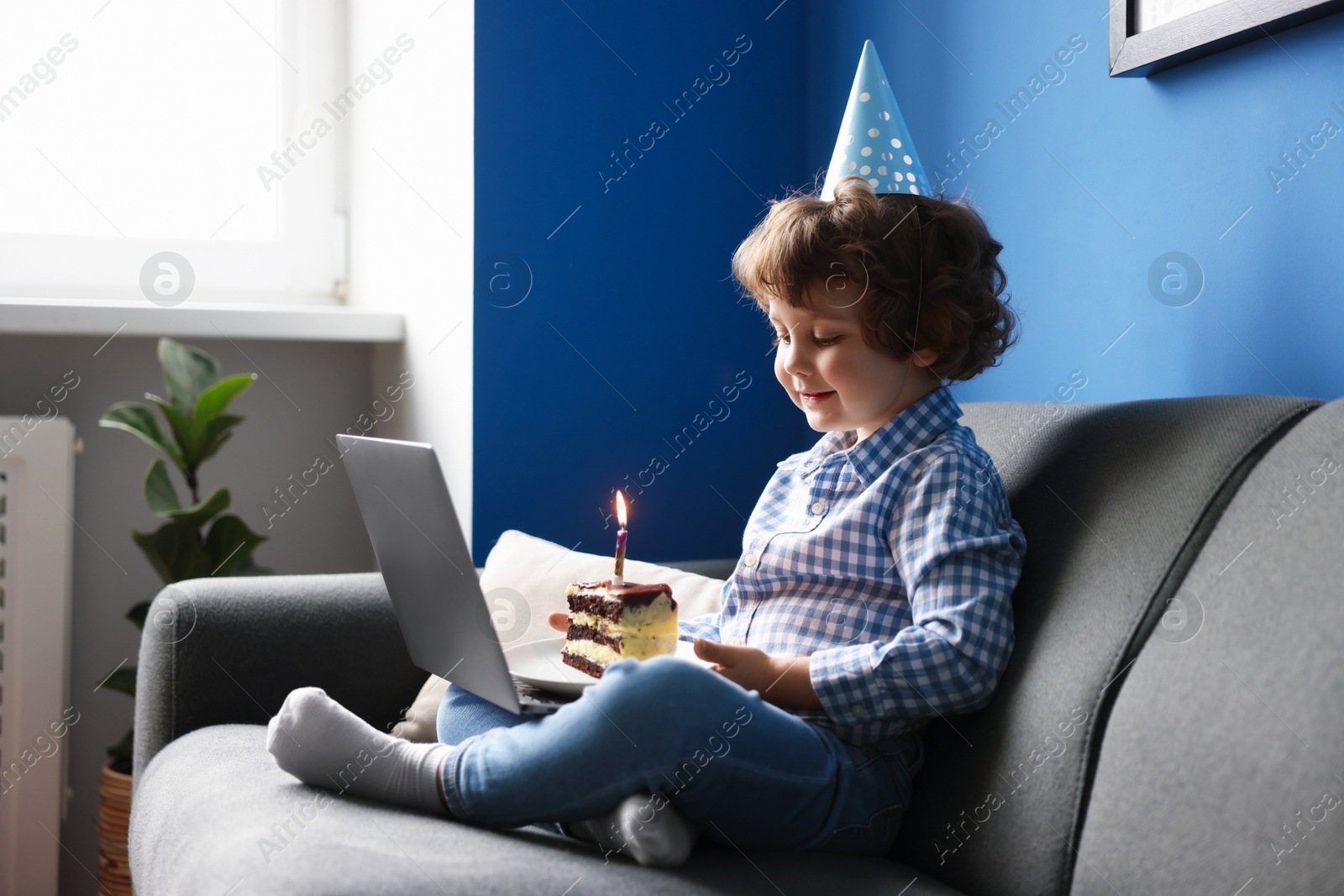 Birthday celebration. Little boy with piece of cake having video call via laptop on sofa at home Photo of Birthday celebration. Little boy with piece of cake having video call via laptop on sofa at home