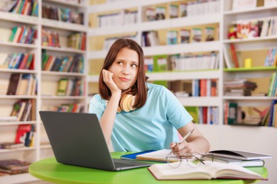 Photo of Student with laptop studying at table in library