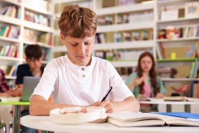 Photo of Student with books studying at table in library