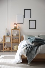 Photo of Cozy bed with soft linens and shelving unit with decor in stylish room. Home textile