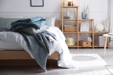 Photo of Cozy bed with soft linens and shelving unit with decor in stylish room. Home textile