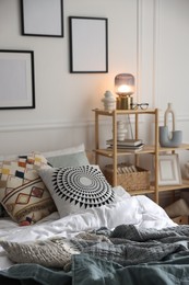 Photo of Cozy bed with soft linens and shelving unit with decor in stylish room. Home textile