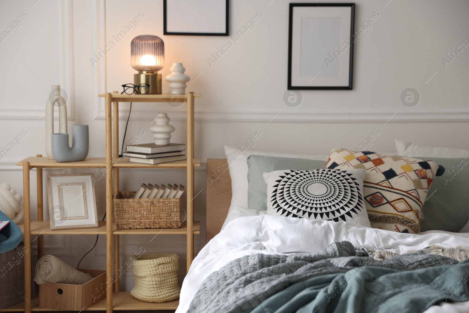 Cozy bed with soft linens and shelving unit with decor in stylish room. Home textile Photo of Cozy bed with soft linens and shelving unit with decor in stylish room. Home textile