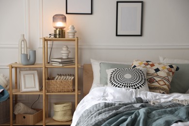 Photo of Cozy bed with soft linens and shelving unit with decor in stylish room. Home textile