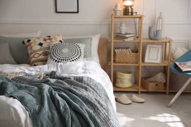Photo of Cozy bed with soft linens and shelving unit with decor in stylish room. Home textile