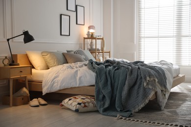 Photo of Cozy bed with soft linens, nightstand and lamp in stylish room. Home textile