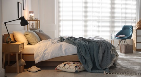 Photo of Cozy bed with soft linens, nightstand and lamp in stylish room. Home textile