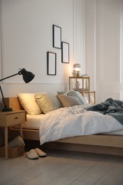 Photo of Cozy bed with soft linens, nightstand and lamp in stylish room. Home textile