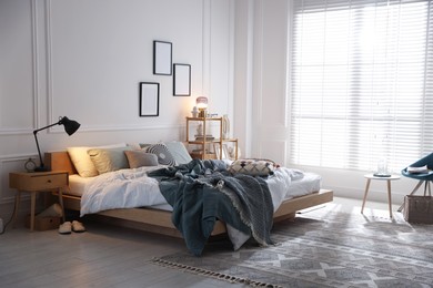 Photo of Cozy bed with soft linens, nightstand and lamp in stylish room. Home textile