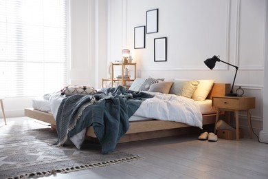 Photo of Cozy bed with soft linens, nightstand and lamp in stylish room. Home textile