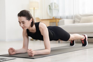 Photo of Woman doing plank exercise during online class with coach at home. Sport and healthy lifestyle