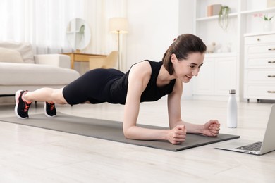 Photo of Woman doing plank exercise during online class with coach at home. Sport and healthy lifestyle