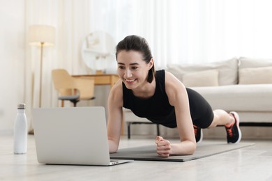 Photo of Woman doing plank exercise during online class with coach at home. Sport and healthy lifestyle
