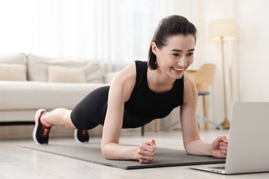 Photo of Woman doing plank exercise during online class with coach at home. Sport and healthy lifestyle