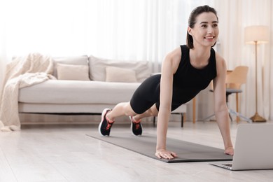 Photo of Woman doing plank exercise during online class with coach at home. Sport and healthy lifestyle