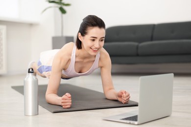 Photo of Woman doing plank exercise during online class with coach at home. Sport and healthy lifestyle