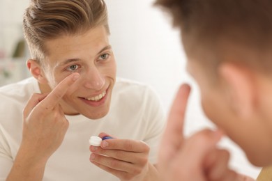 Photo of Man putting in contact lens near mirror at home