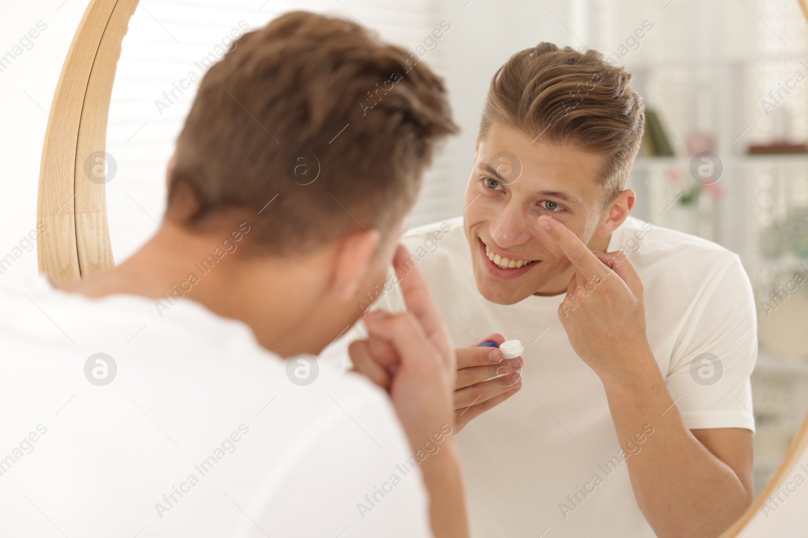 Man putting in contact lens near mirror at home Photo of Man putting in contact lens near mirror at home