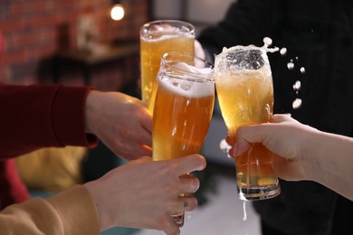 Photo of Friends clinking glasses of beer indoors, closeup