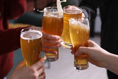 Photo of Friends clinking glasses of beer indoors, closeup